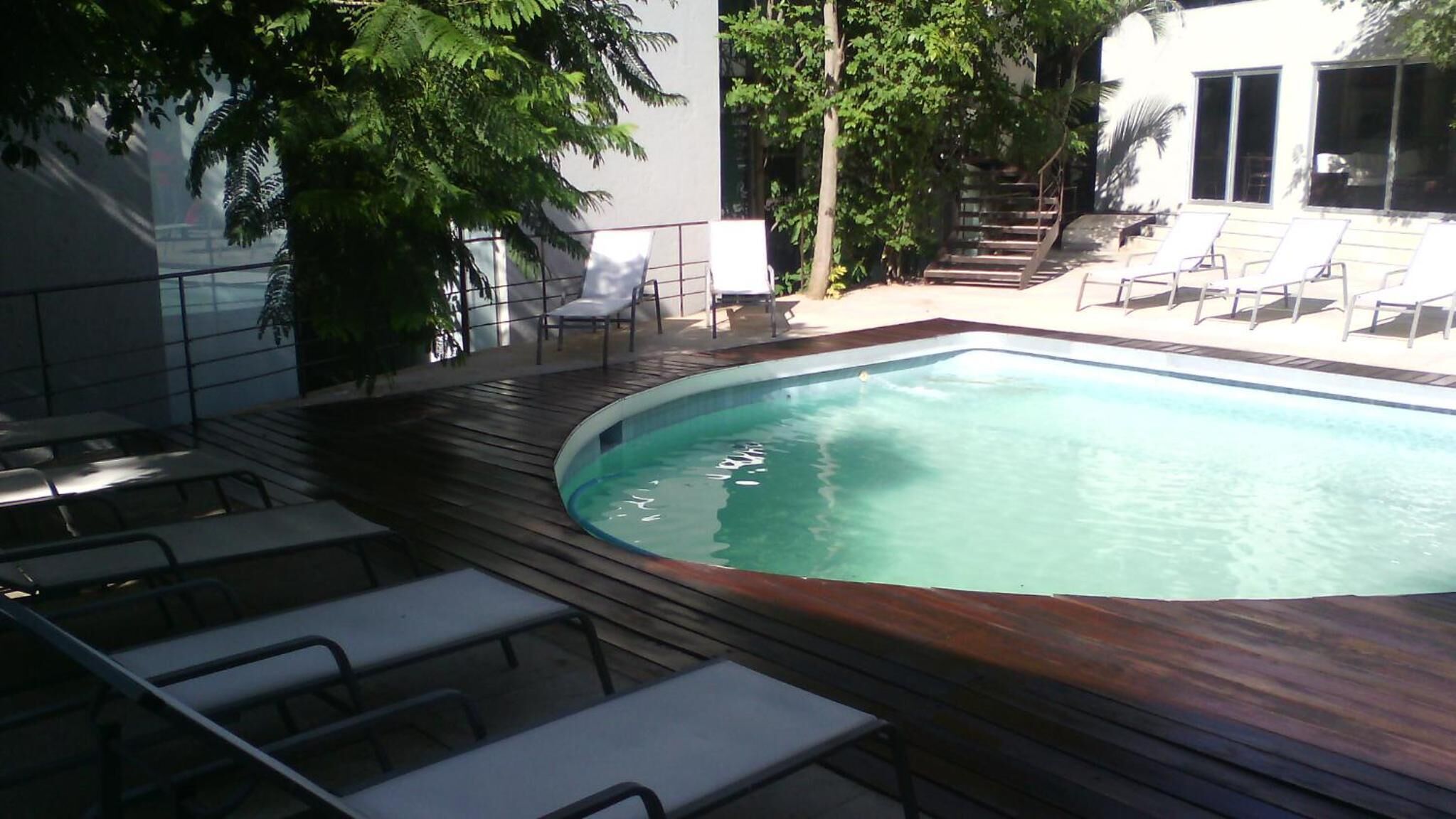 Ein rechteckiger Pool mit einer umlaufenden Holzterrasse, ausgestattet mit weißen Liegestühlen und einer Treppe zu einer erhöhten Ebene.