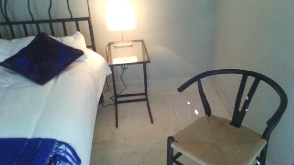 Un dormitorio con una cama, una mesita, una silla y una mesita de noche con lámpara.