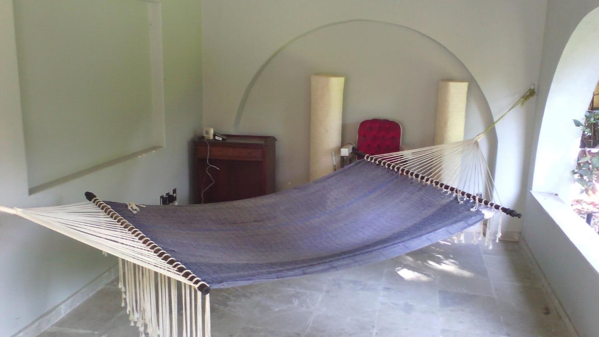 Una hamaca en una habitación con suelo de baldosas, un armario de madera y una silla roja.