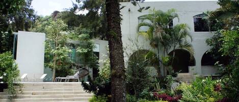 A modern building with a white exterior, surrounded by lush greenery and a well-maintained lawn.