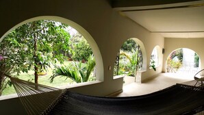 A hammock in a room with arched windows overlooking a garden.