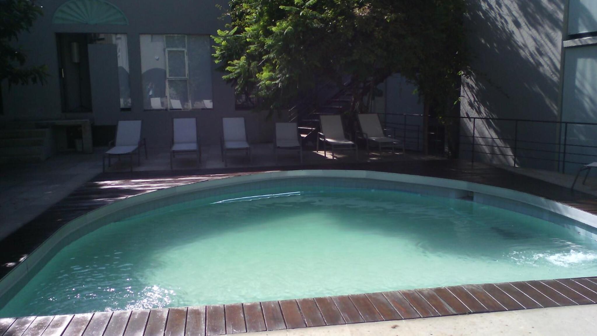Una piscina con cubierta de madera, rodeada de sillas de descanso y un edificio con ventanas.