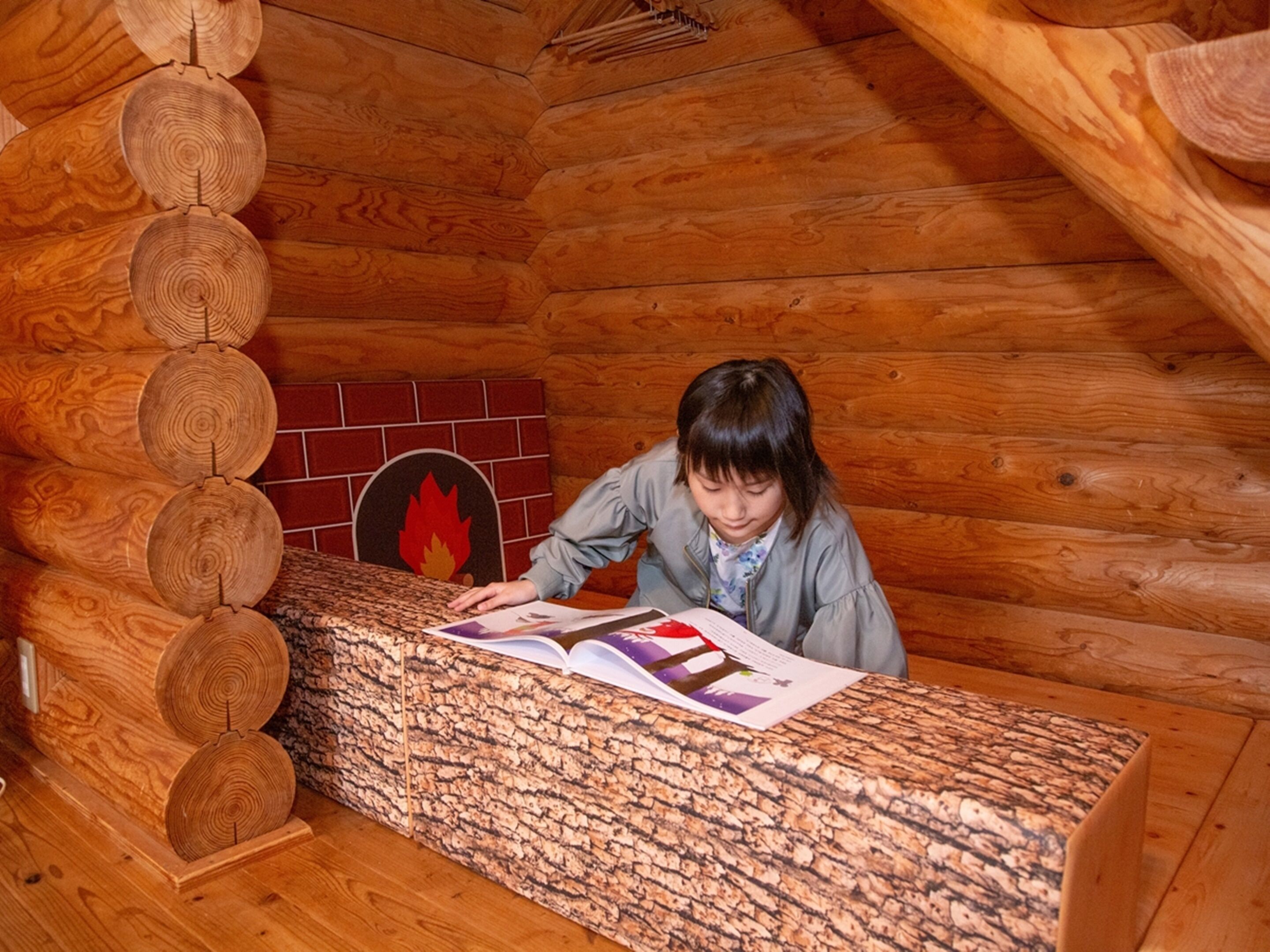 Ein Blockhaus-Interieur mit einer Holzwand aus Baumstämmen, einem Kamin und einer Person, die ein Buch liest.