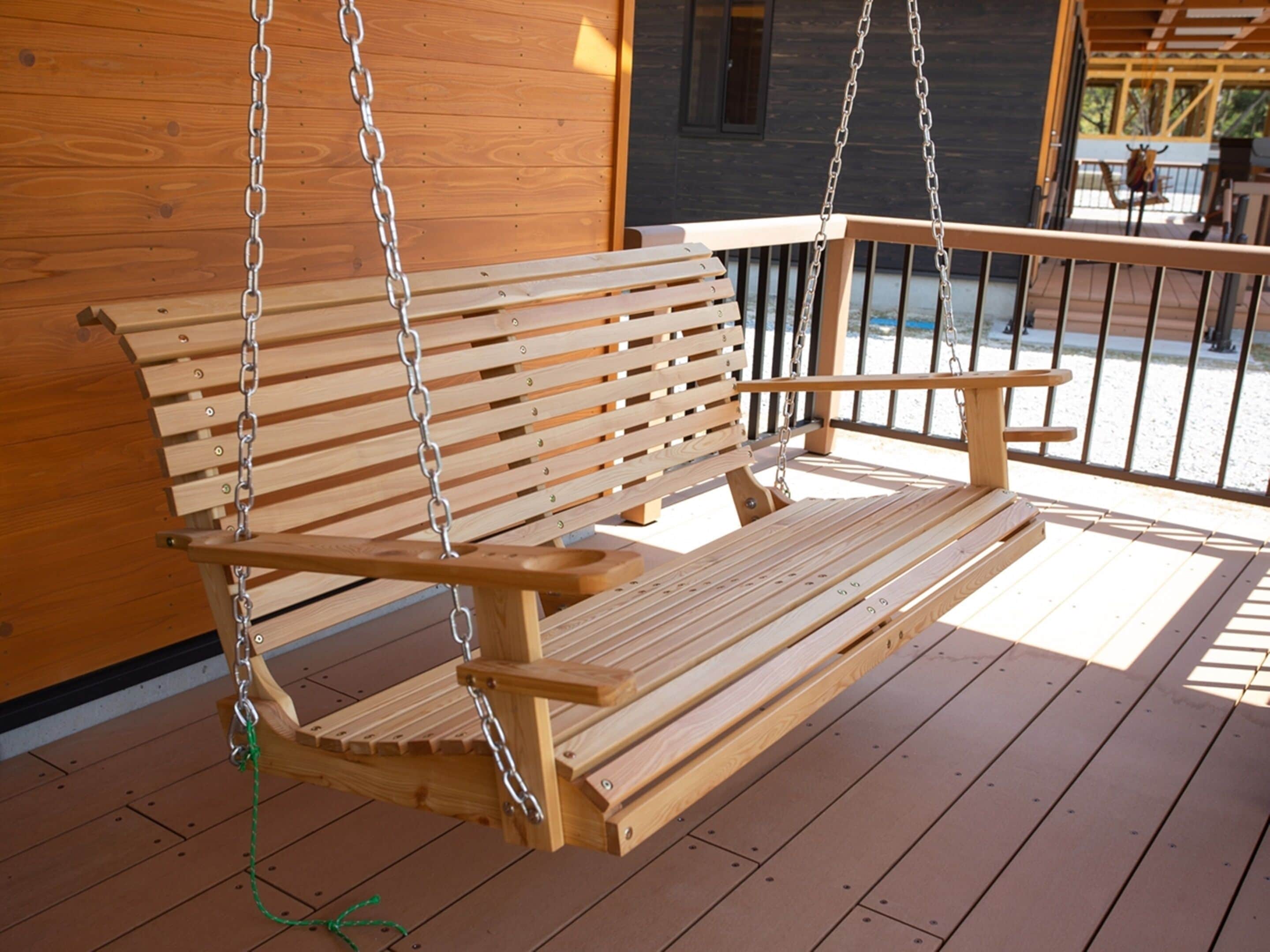 A wooden swing bench with metal chains, suspended over a wooden deck.