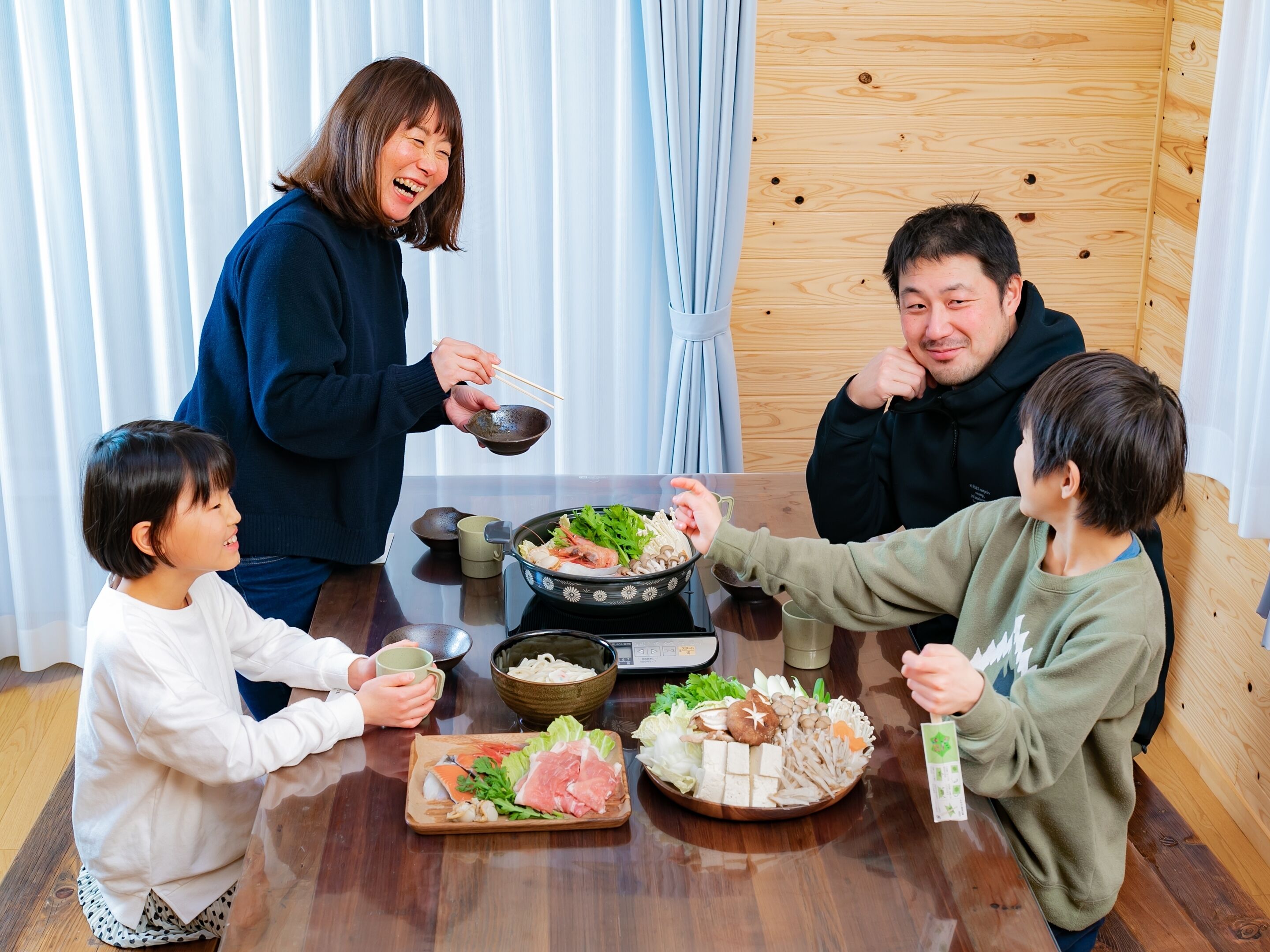 Una familia cenando en una mesa de madera con diversos platos, incluyendo mariscos y verduras.