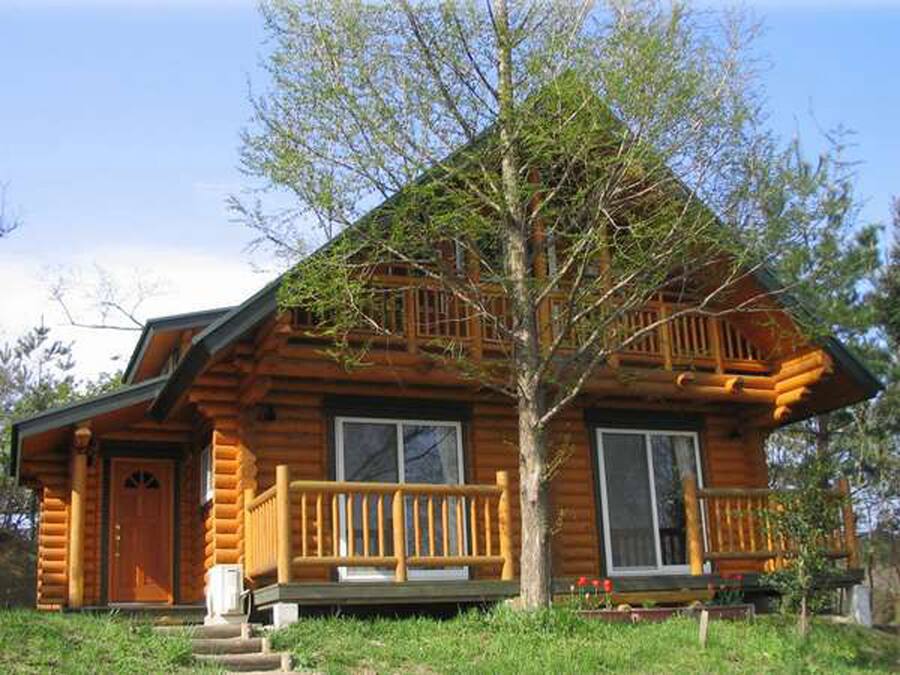 A log cabin with a front porch, large windows, and a wooden deck.
