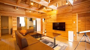 L’intérieur chaleureux d’un chalet avec un grand plafond en bois, un canapé, une table à manger et un téléviseur fixé au mur.