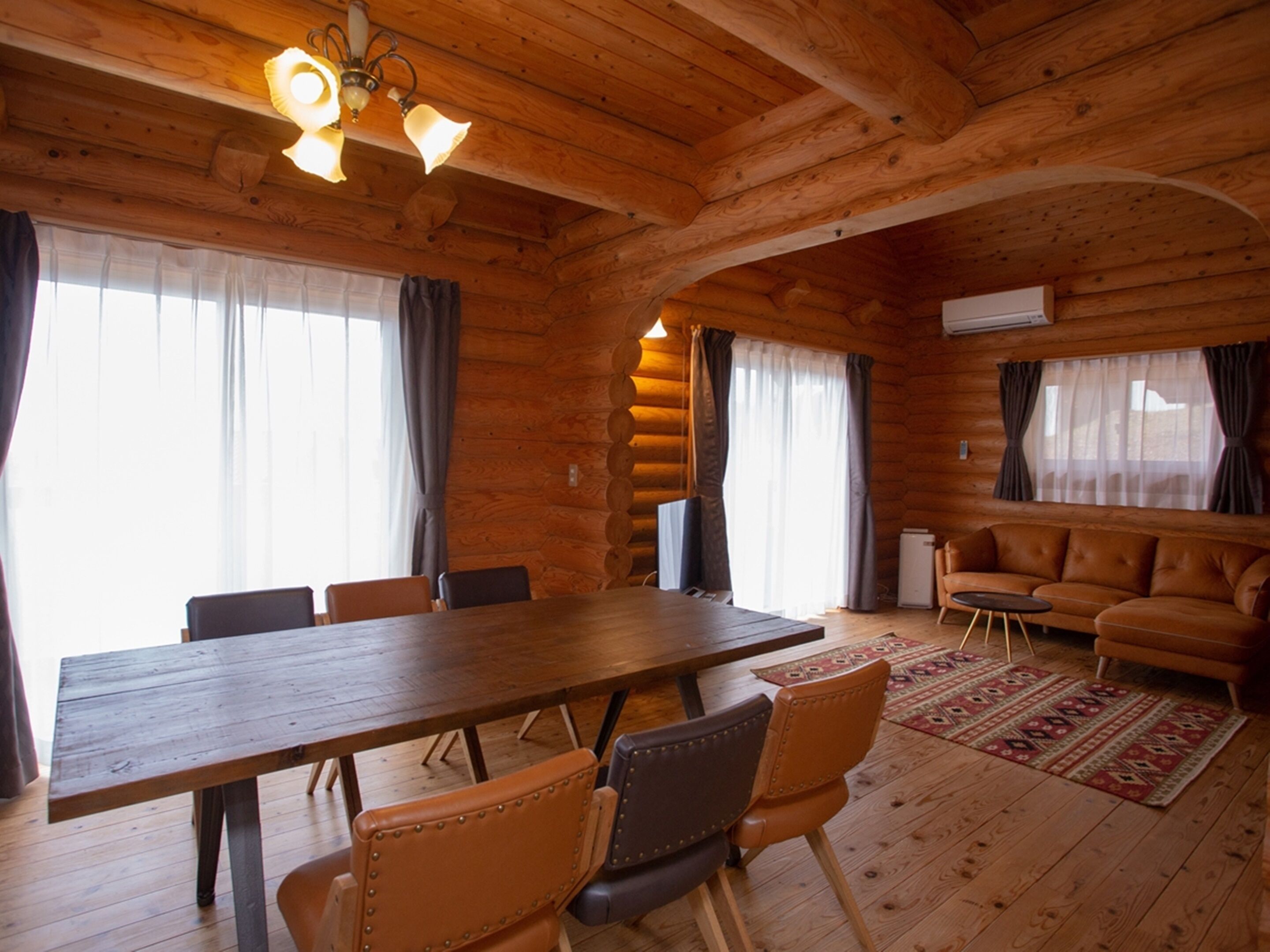 Een blokhutinterieur met een houten eettafel, lederen stoelen, een lederen bank en een open haard.