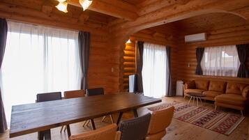 Een blokhutinterieur met een houten eettafel, lederen stoelen, een lederen bank en een open haard.