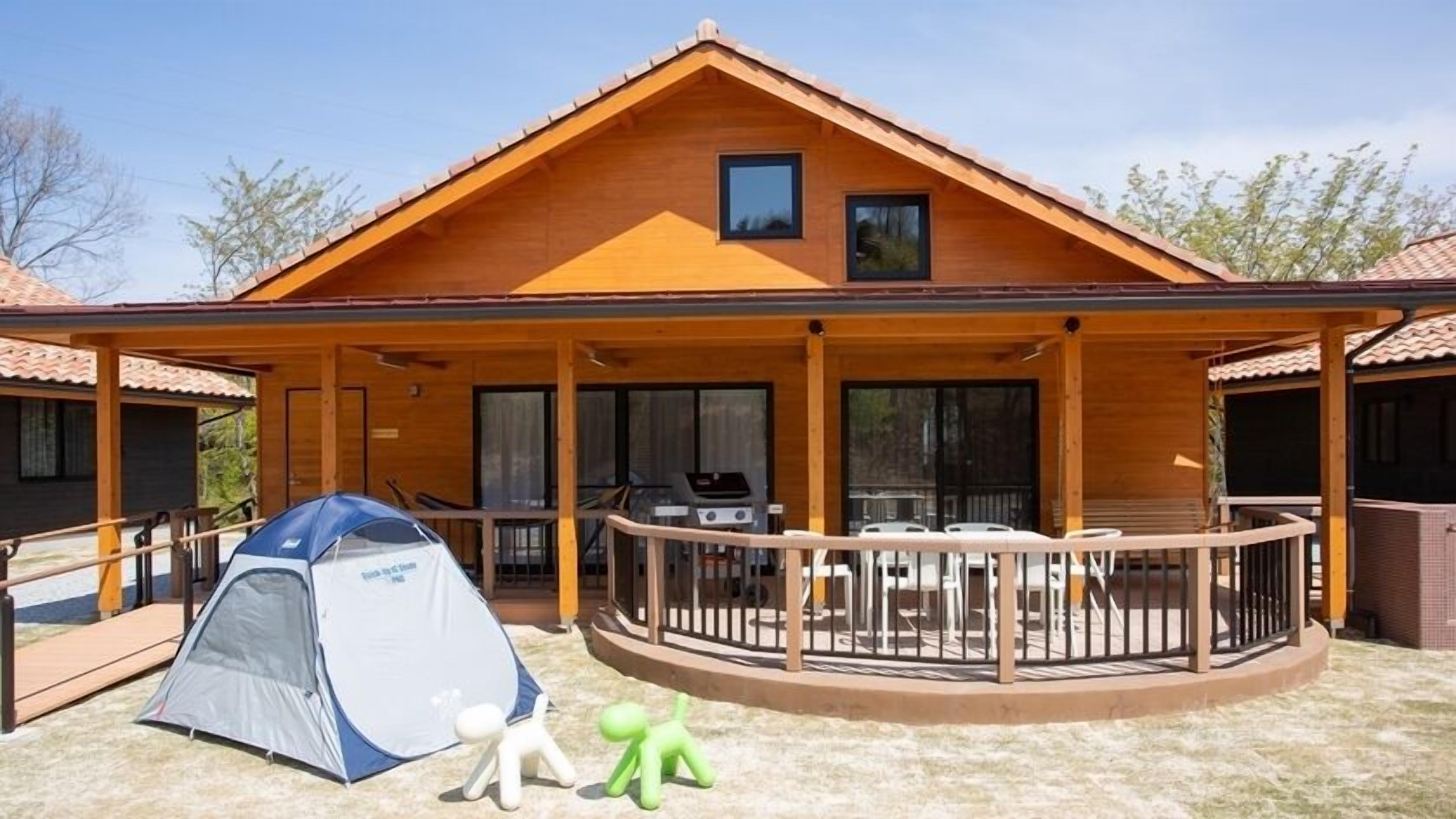 Eine Holzhütte mit Veranda, Grill und Zelt.