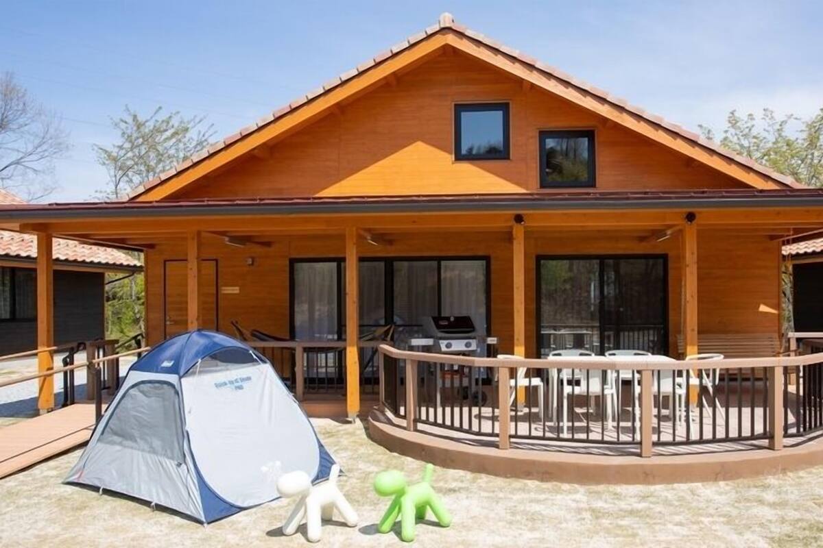 Une cabane en bois avec un porche couvert, un barbecue et une tente.