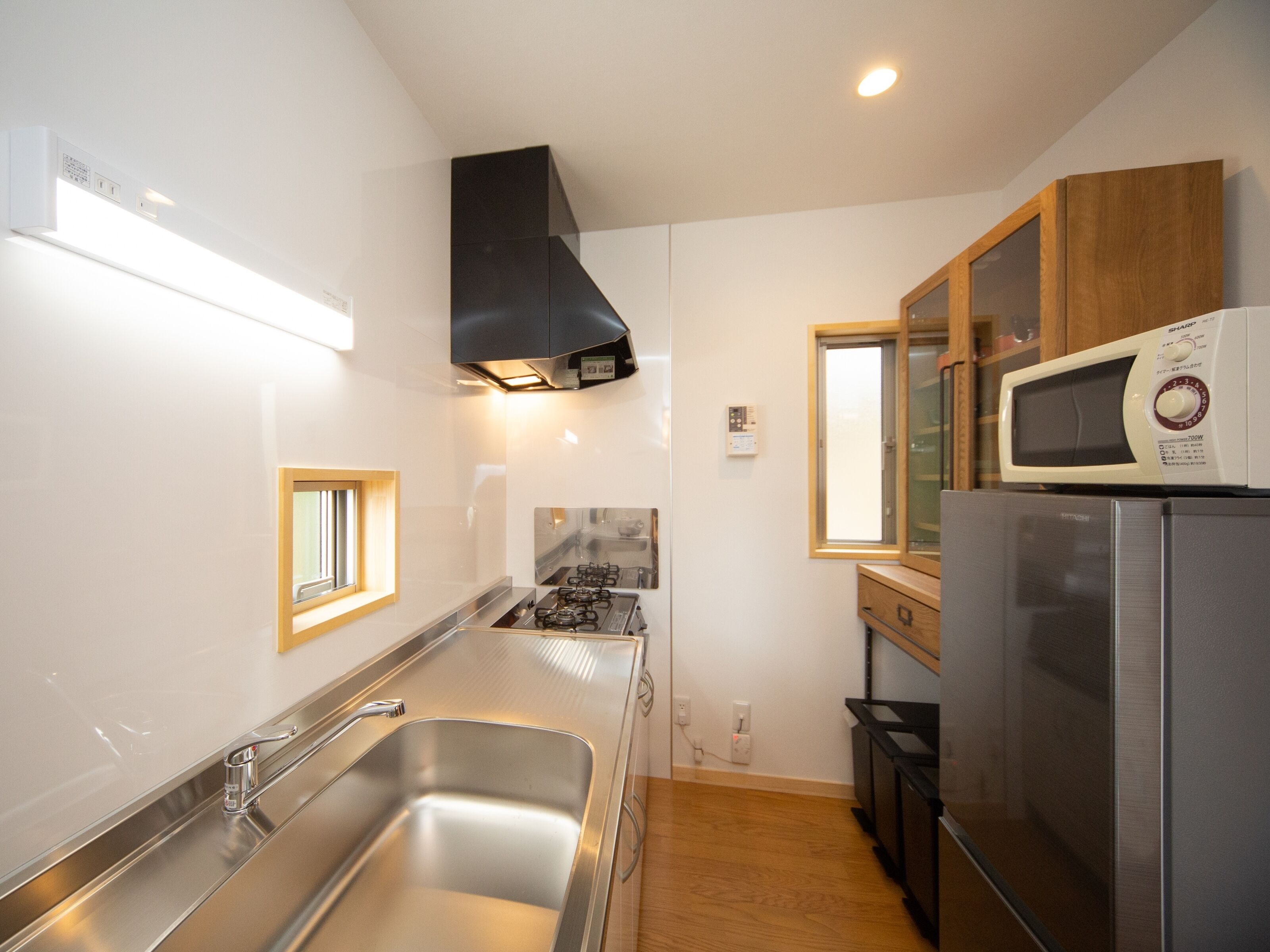 A compact kitchen with a stainless steel sink, a gas stove, a black range hood, and a microwave on top of a refrigerator.