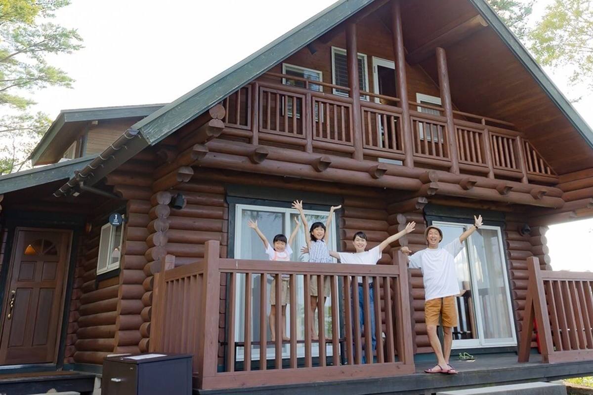 Une cabane en rondins avec un balcon, une porte d’entrée et une fenêtre.