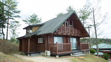 A two-story log cabin with a balcony, a front porch, and a small front yard.