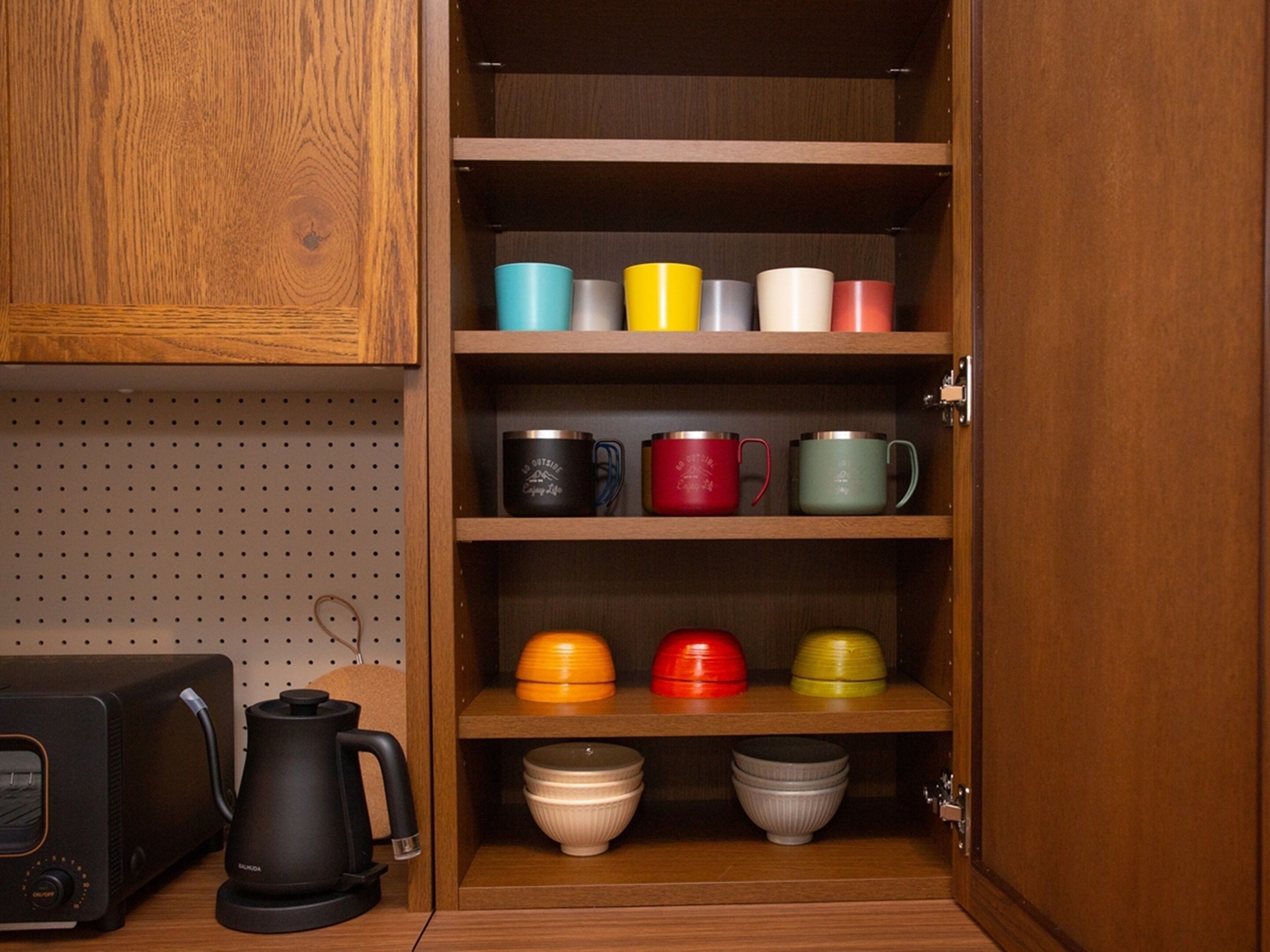 Un armario de madera con estantes que contienen tazas y cuencos de colores variados.