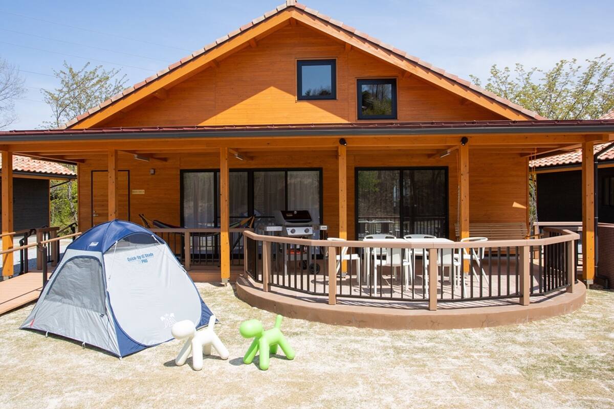 Une cabane en bois avec une véranda, un barbecue et une tente.