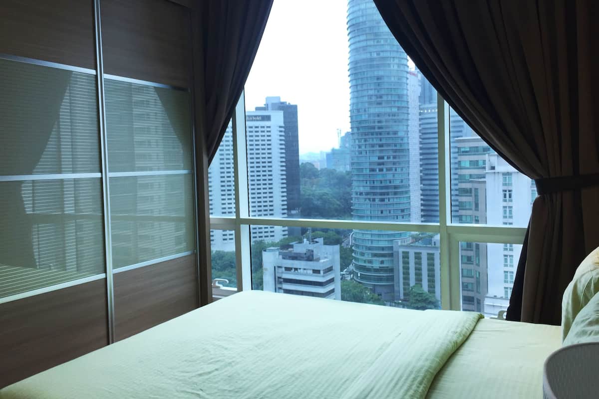 A bedroom with a large window, a bed, and a view of tall buildings.