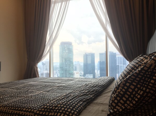 Una cama con una manta y almohadas estampadas, una ventana con cortinas y vistas a la ciudad.