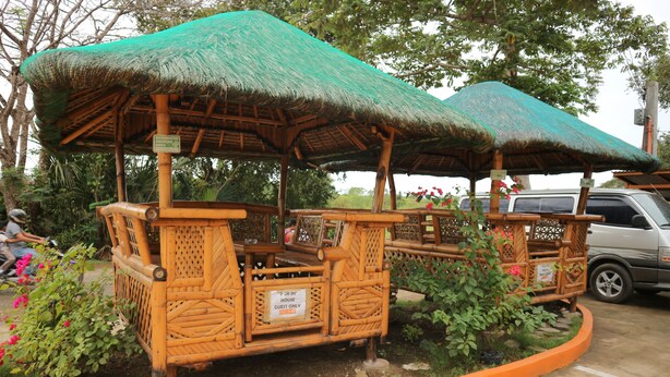 Un kiosque en bois avec un toit de chaume, entouré d’une bordure circulaire en pierre, et une pancarte indiquant qu’il est réservé aux clients.