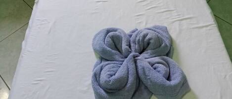 A single bed with a white mattress and a blue towel folded in a flower shape.