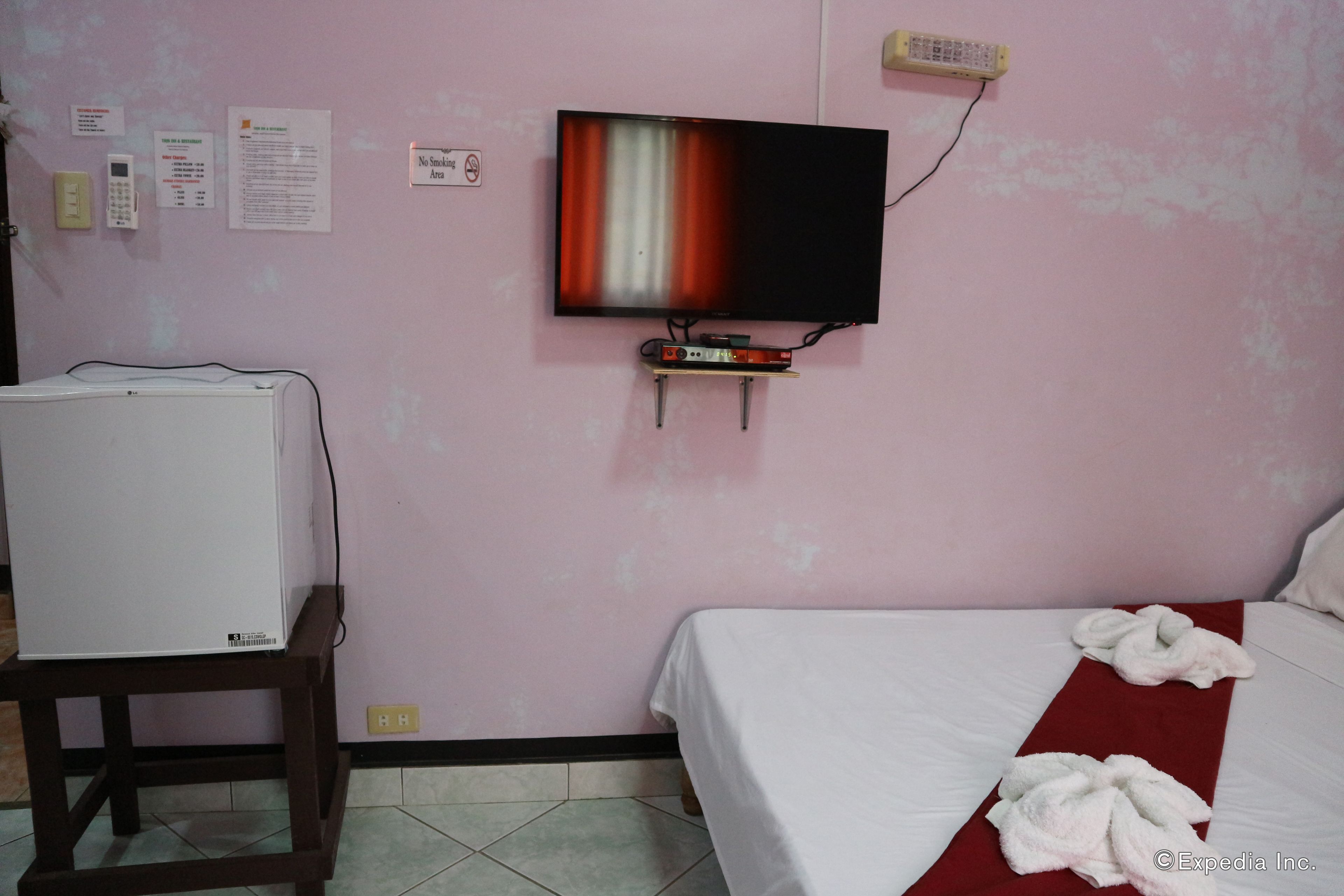 Een hotelkamer met een bed, een aan de muur bevestigde televisie, een klein tafeltje met een televisie en een rode handdoek op het bed.