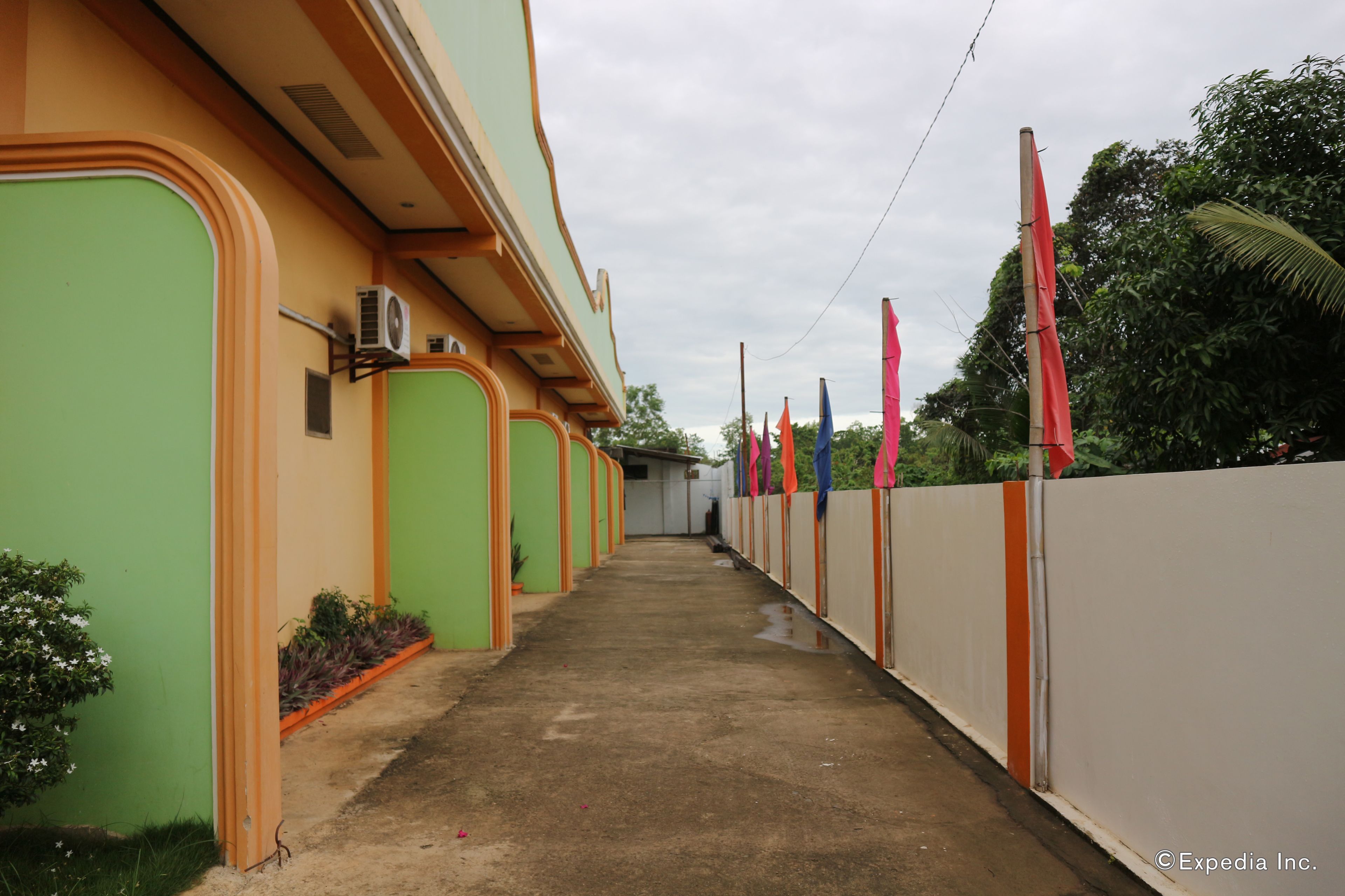 A corridor with green and orange walls, a concrete floor, and a white fence with colorful flags.