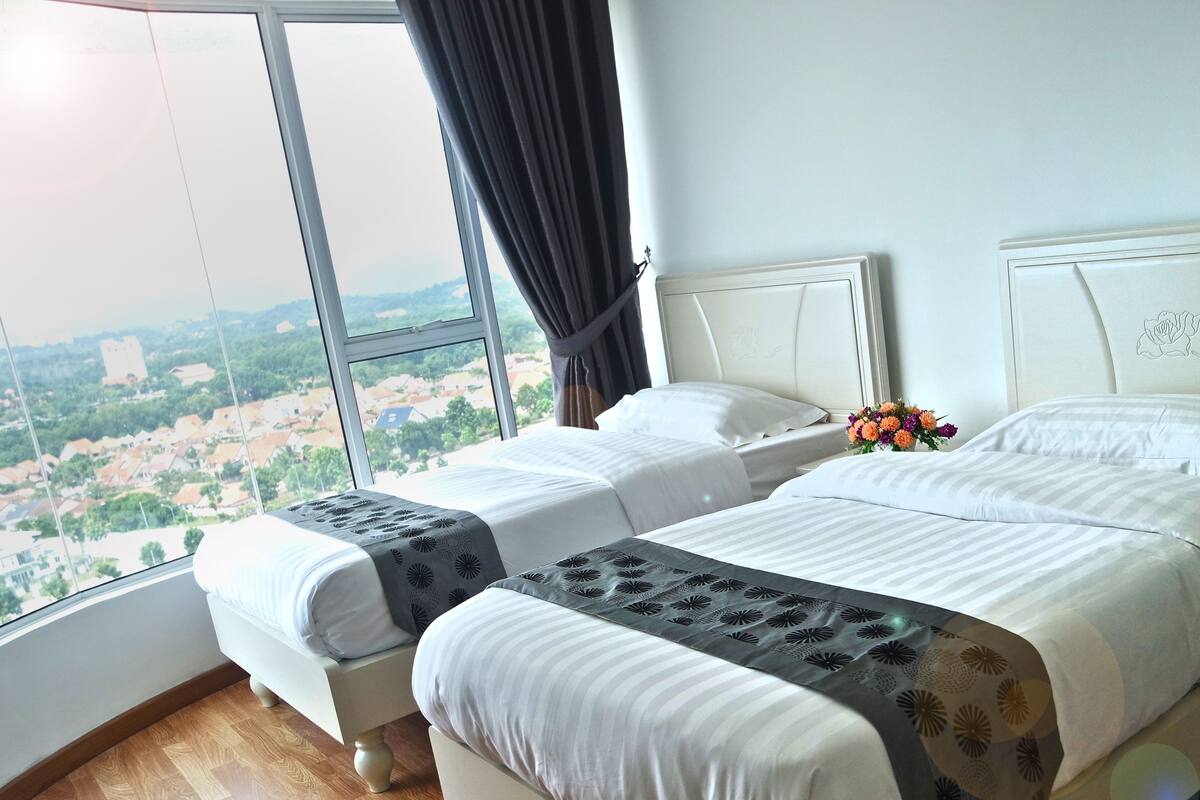 Ein Hotelzimmer mit zwei Betten, einem großen Fenster und Blick auf eine Stadtlandschaft.