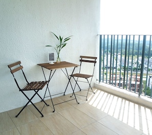 Un balcon avec une table en bois et deux chaises, un pot de fleurs et une vue sur le paysage urbain.