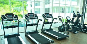 Une rangée de tapis de course dans une salle de sport dotée de grandes fenêtres et offrant une vue sur la verdure environnante.