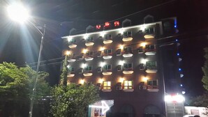 Un hotel de varios pisos con balcones, ventanas iluminadas y un cartel visible sobre la entrada.