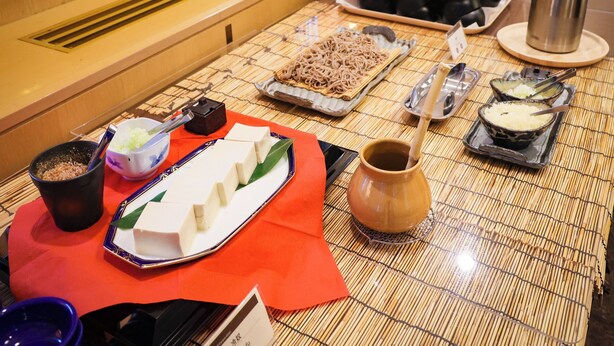 A table with various food items and utensils, including a bowl of noodles, a plate of tofu, and several teapots. - APA Hotel TKP Sapporoeki-Kitaguchi EXCELLENT (Sapporo)