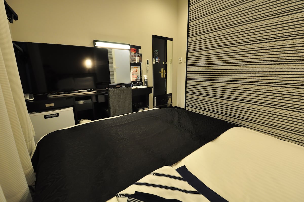 Ein Hotelzimmer mit einem Bett, einem Schreibtisch mit Computer, einem Fernseher und einem Spiegel.
