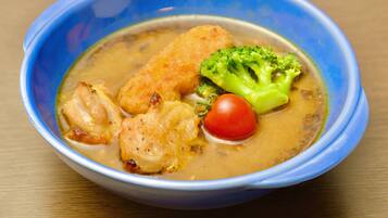 A bowl of soup with chicken, broccoli, and a cherry tomato.