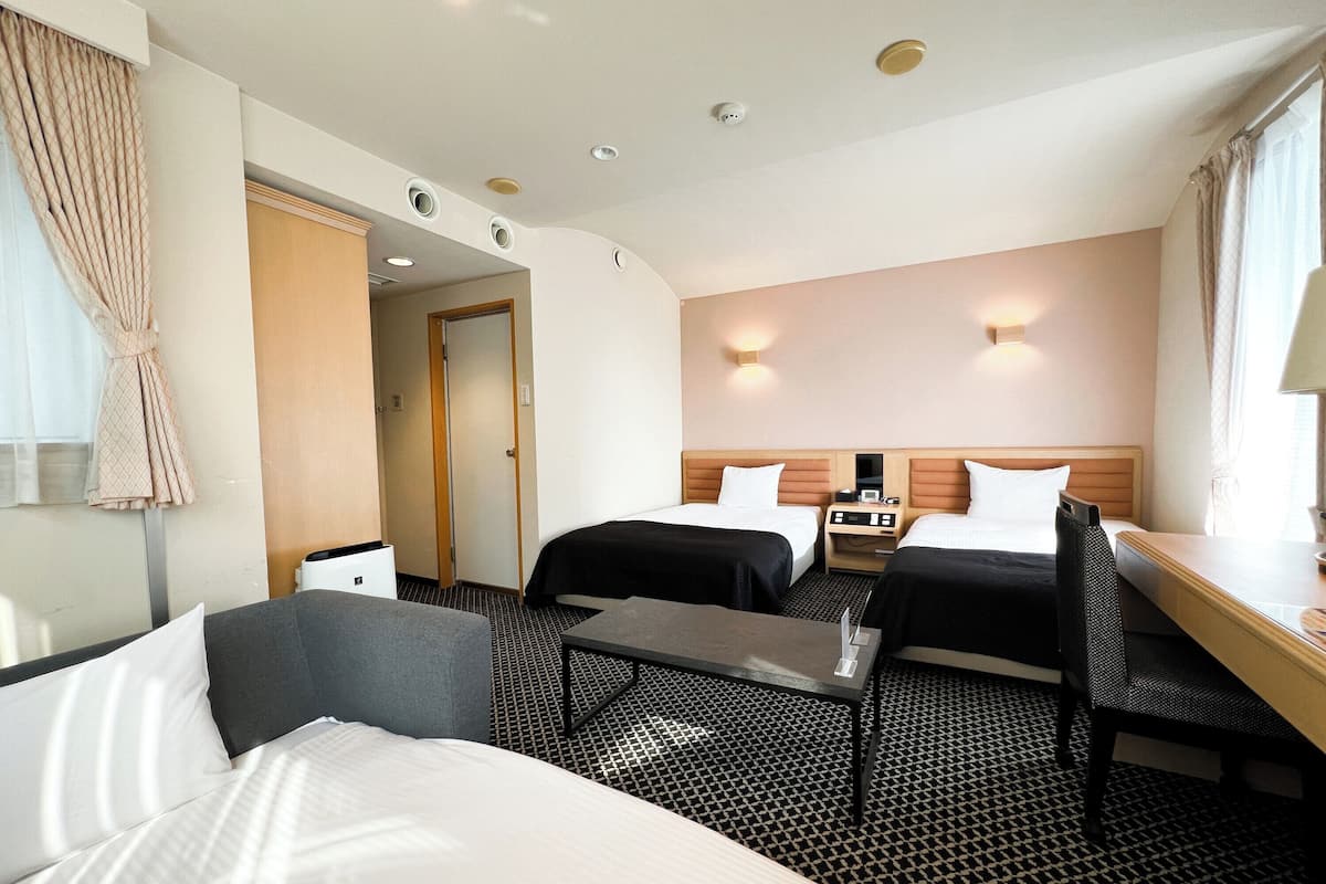 Ein Hotelzimmer mit zwei Betten, einem Schreibtisch, einem Stuhl, einem kleinen Tisch und einer Badezimmertür.