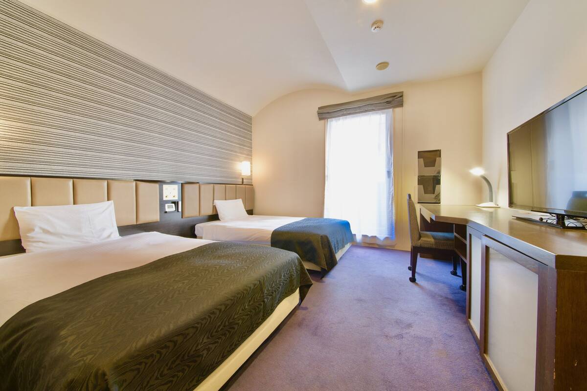 Ein Hotelzimmer mit zwei Betten, einem Schreibtisch und einem Fernseher.
