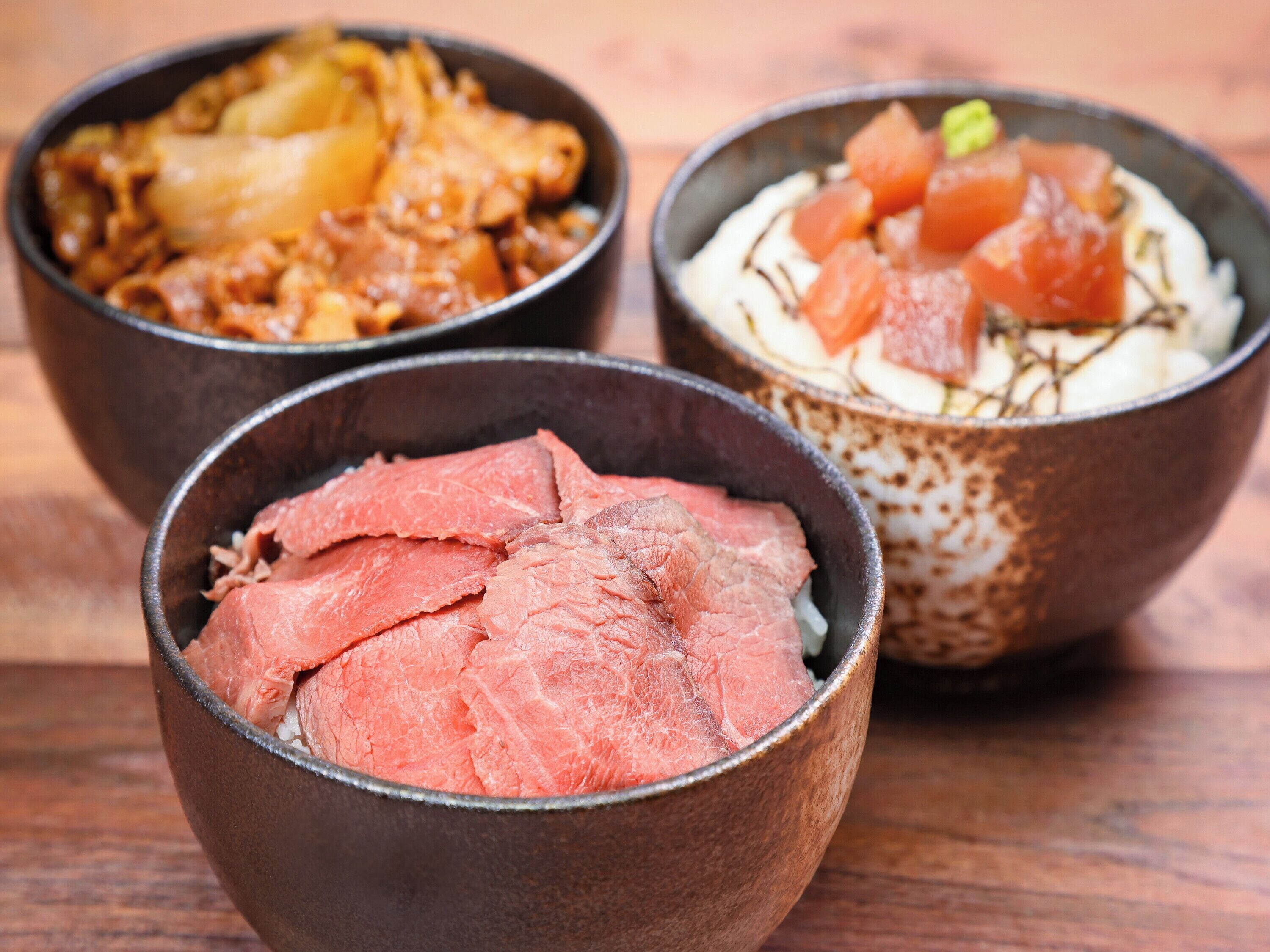 Three bowls of food on a wooden table.