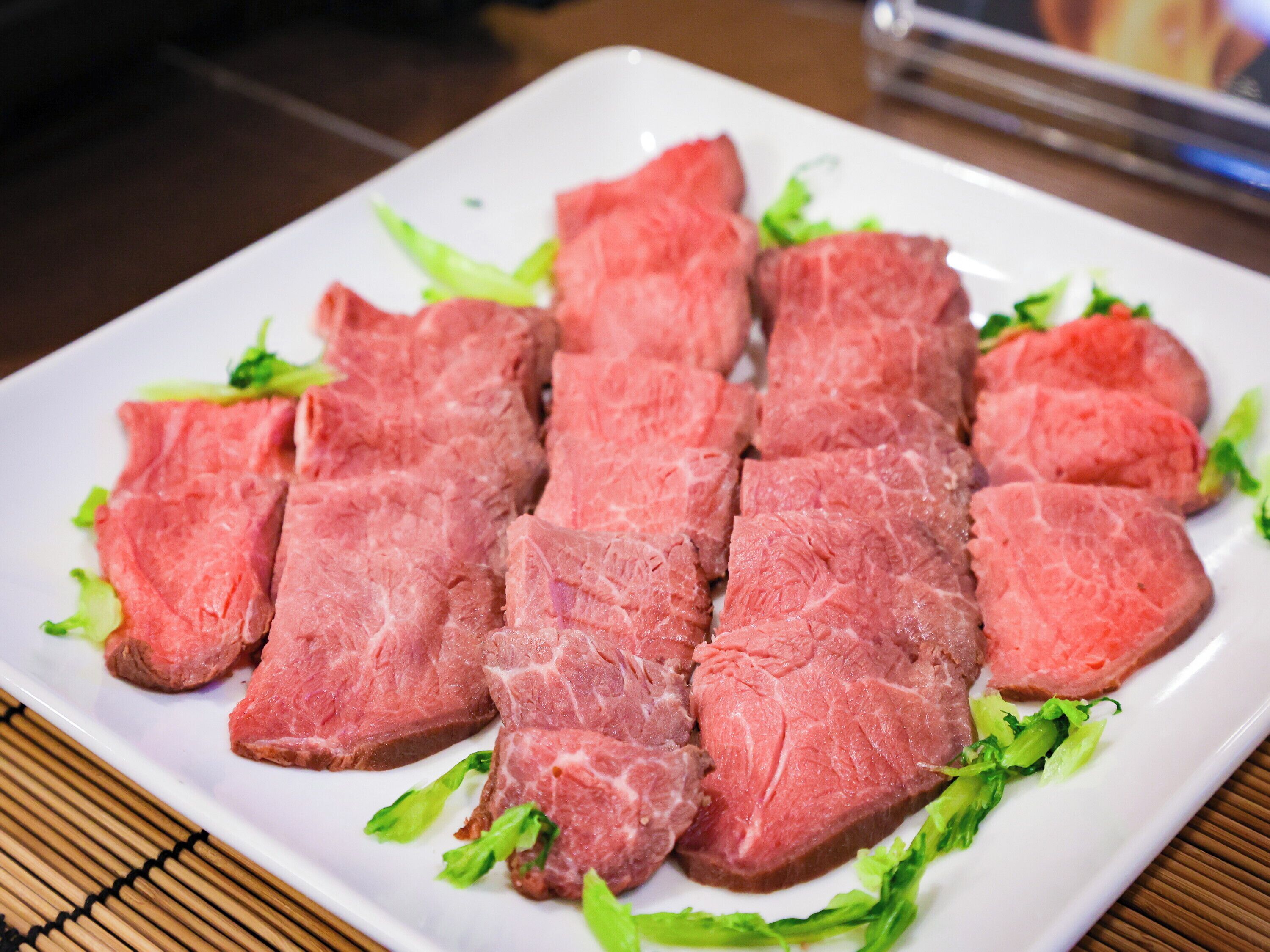 Un plato blanco con lonchas de carne cruda y lechuga verde.