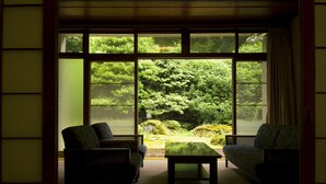 Habitación con un amplio ventanal que ofrece vistas a un jardín. Hay dos sillas y una mesita en la habitación.