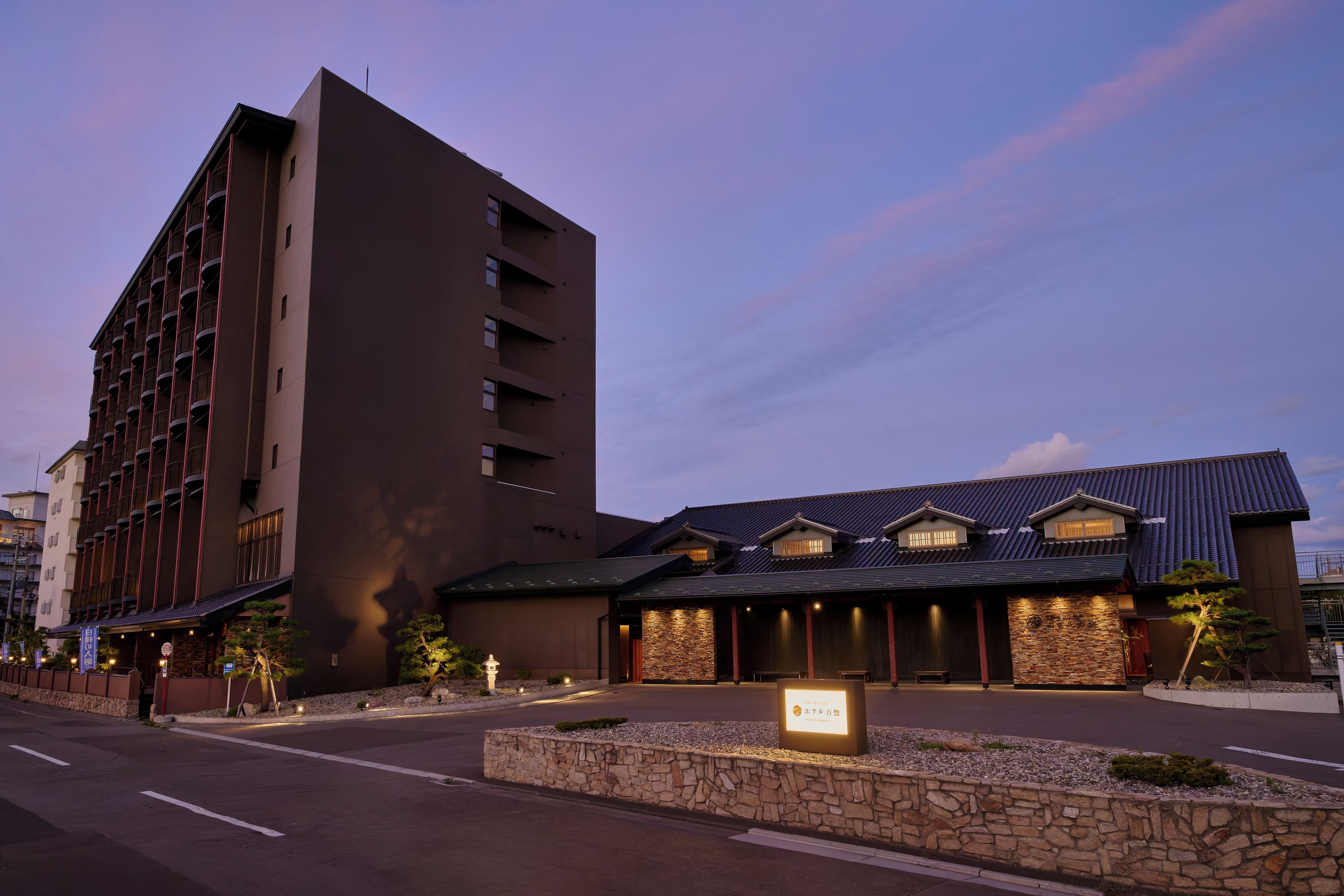 Un hotel con diseño moderno, que presenta un edificio grande de varios pisos y un anexo más pequeño con techo tradicional.