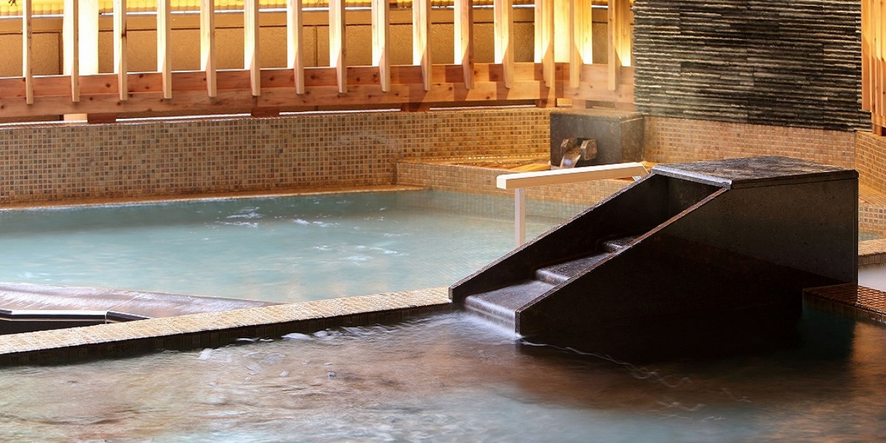 Baño de aguas termales con terraza de madera y pared de piedra.