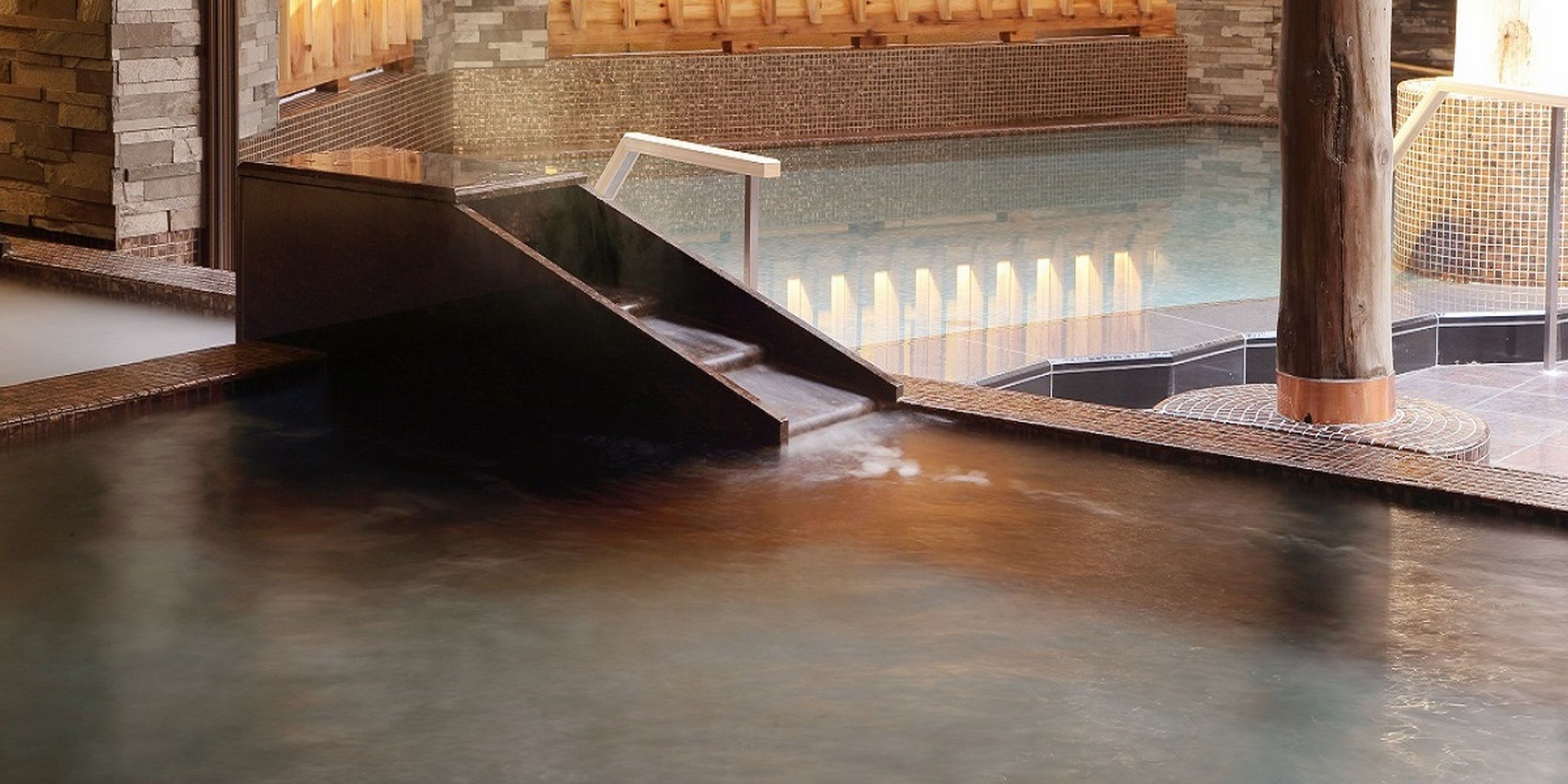 A hot spring area with a wooden deck and a stone wall in the background.