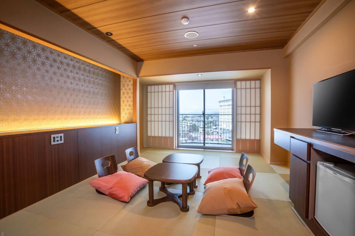 A room with a wooden ceiling, a dining table with chairs, a television, and a view through a large window.