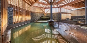 Un spa con una amplia piscina interior, vigas de madera, paredes de piedra y una chimenea de piedra.