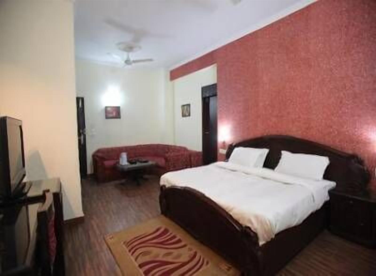 A hotel room with a bed, a TV, a red sofa, and a ceiling fan.
