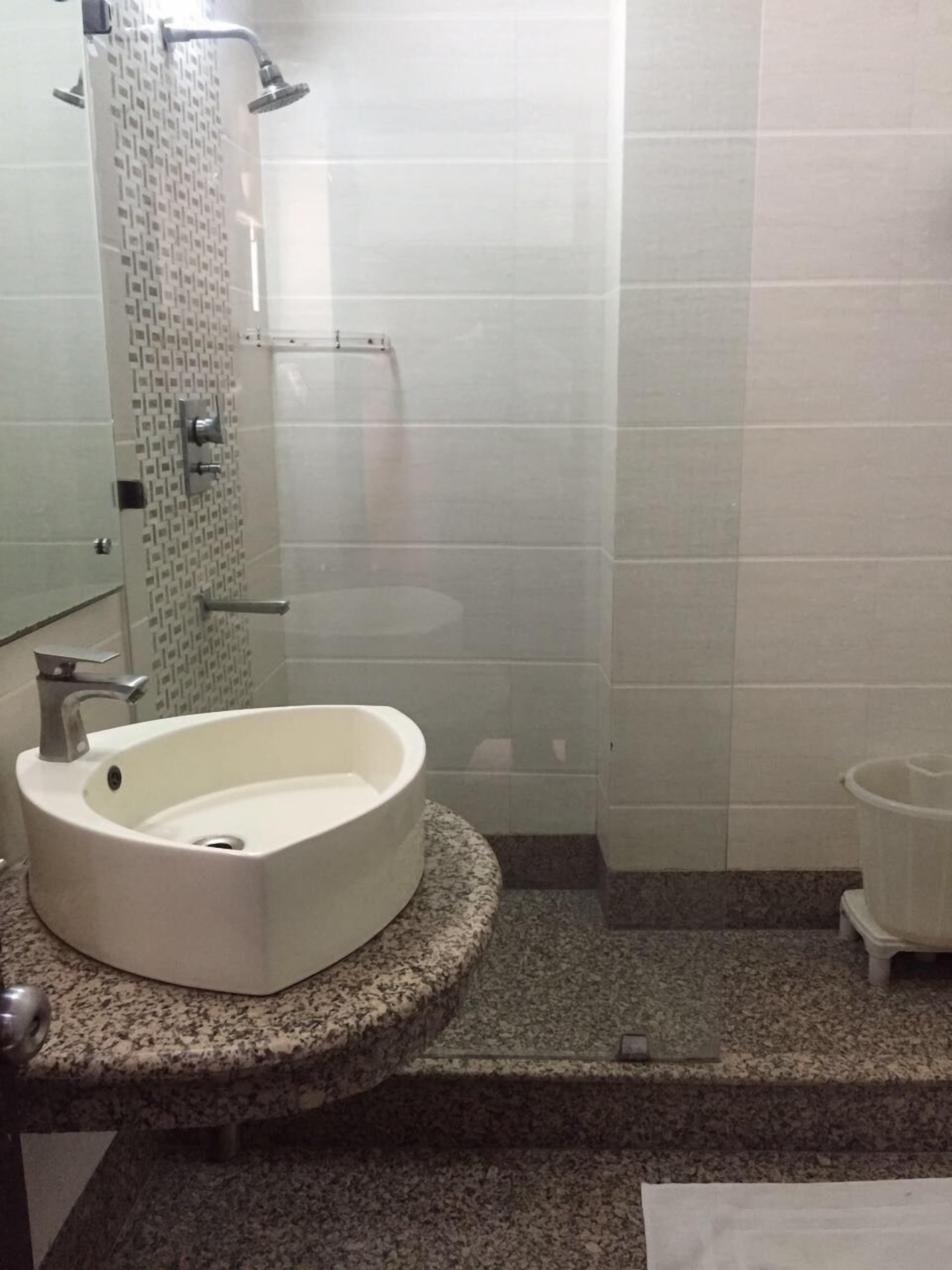 A bathroom with a white sink, a shower, and a granite countertop.