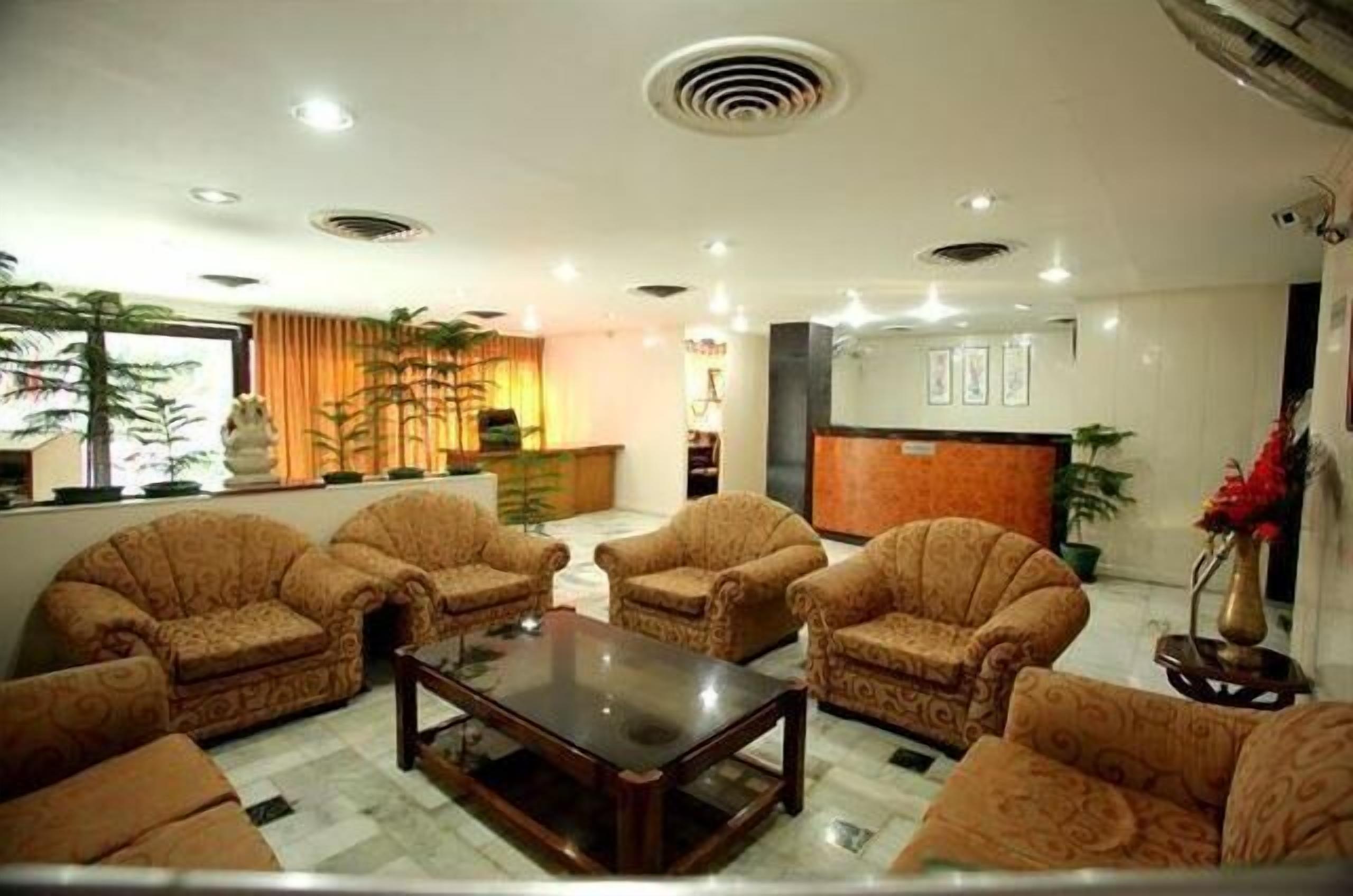 Um saguão de hotel com sofás estampados, uma mesa de centro de vidro e um balcão de recepção.