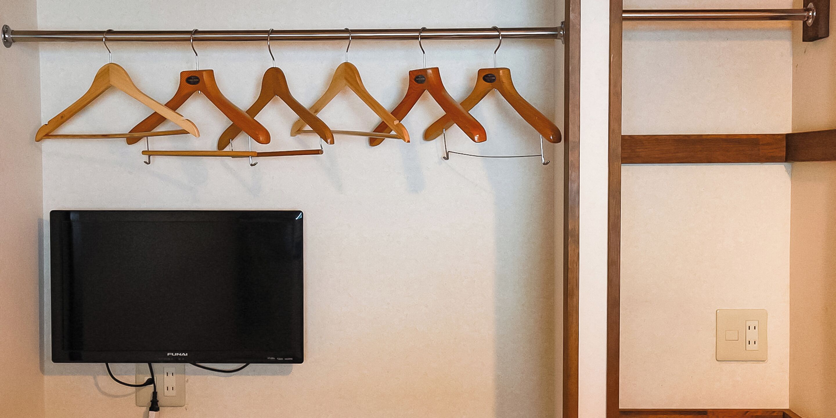 A wall-mounted TV and wooden hangers on a metal rod.