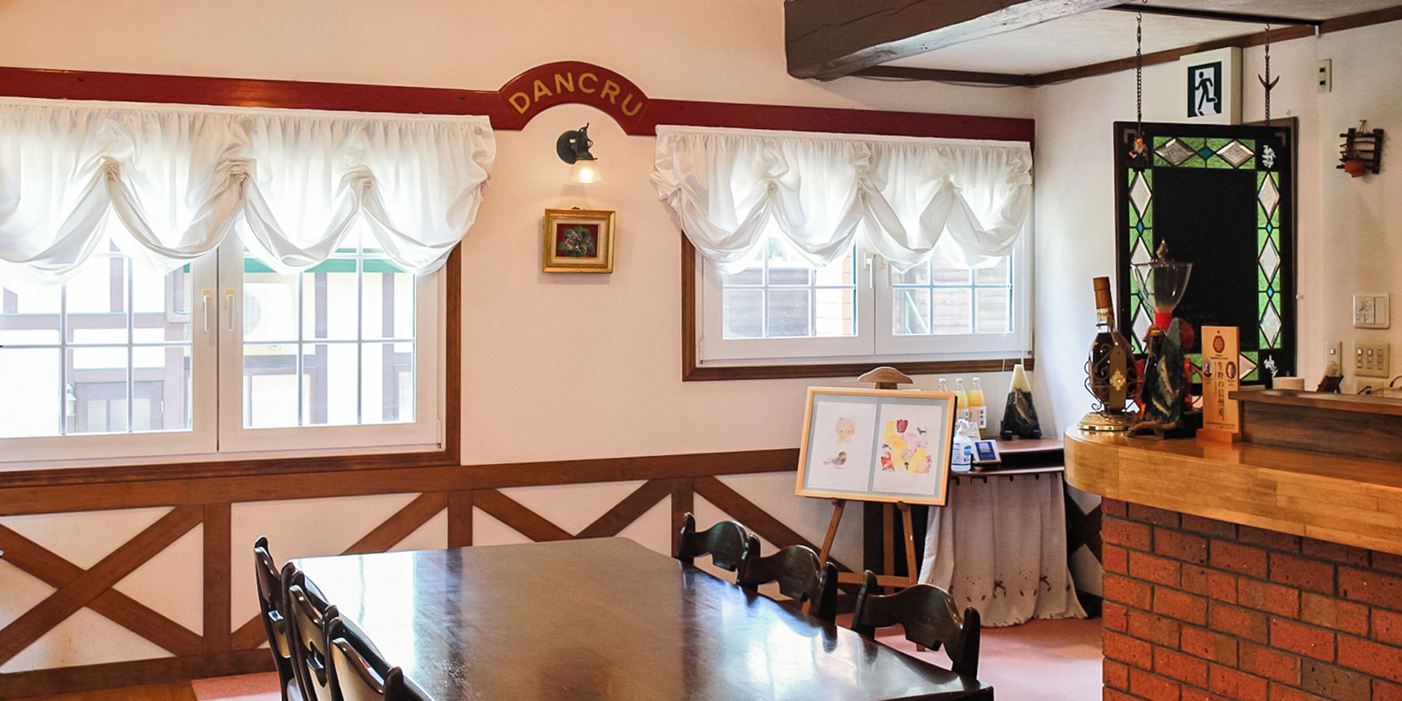 A dining area with a wooden table and chairs, a counter with a cash register, and a sign above the windows reading "DANCRU".