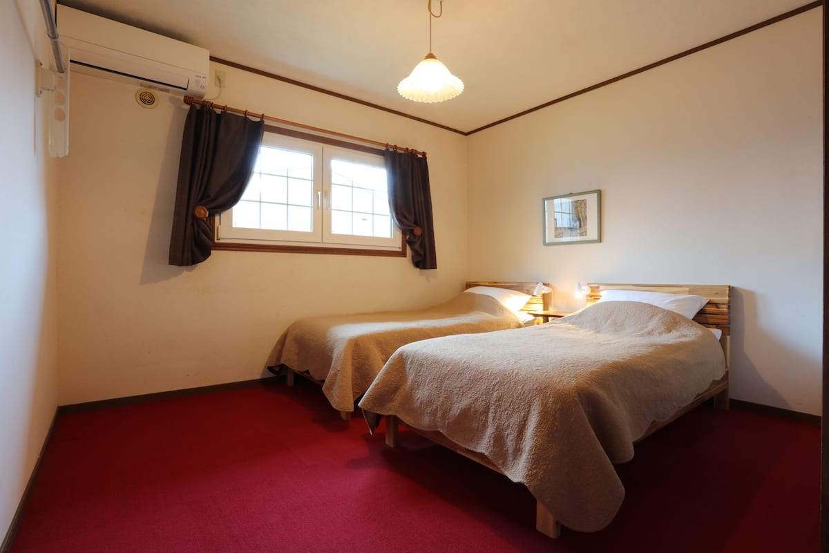 A room with two beds, a window with curtains, a wall-mounted air conditioner, and a framed picture.