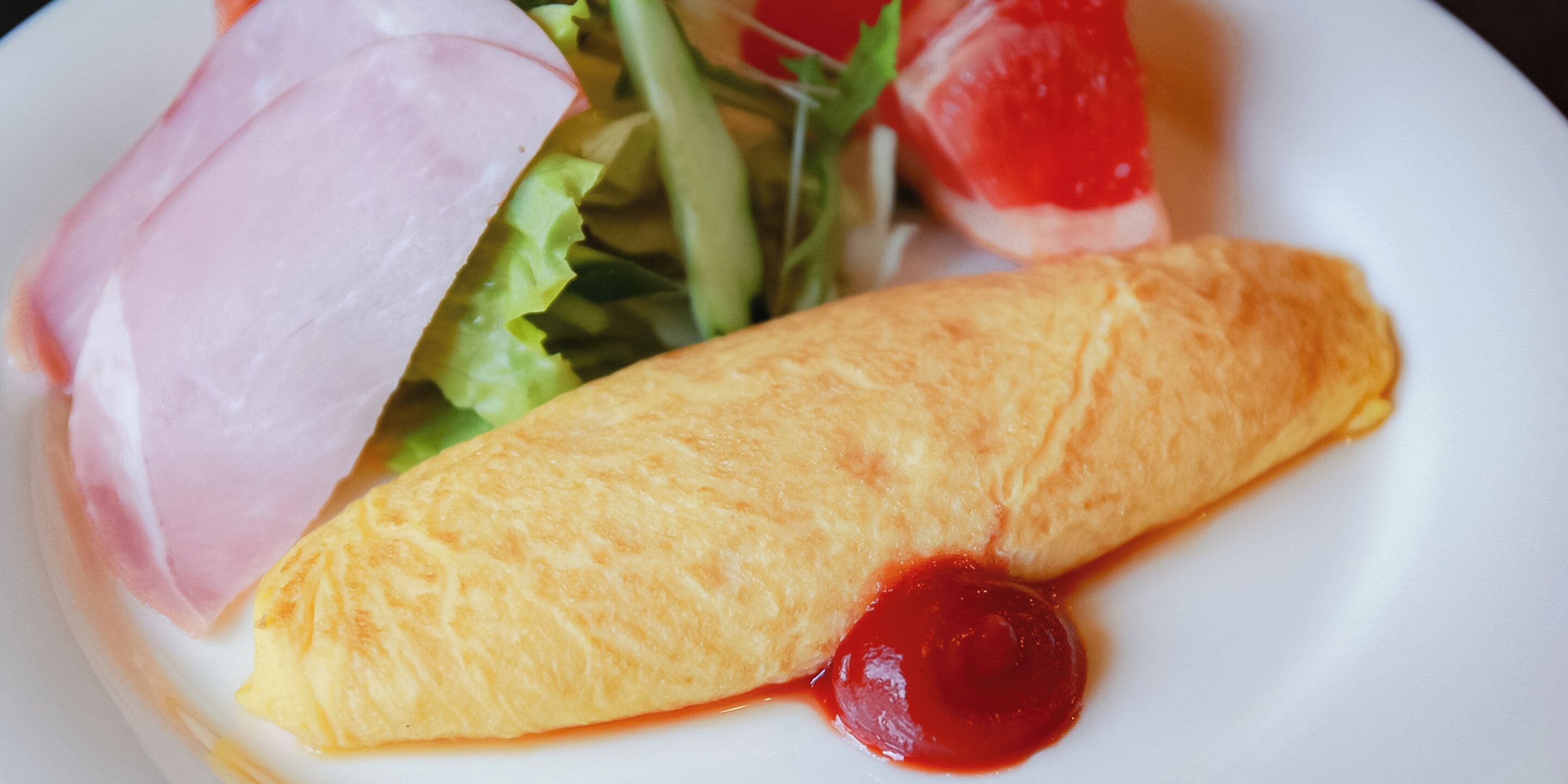 Un plato con una tortilla enrollada, una loncha de jamón, lechuga y salsa roja.